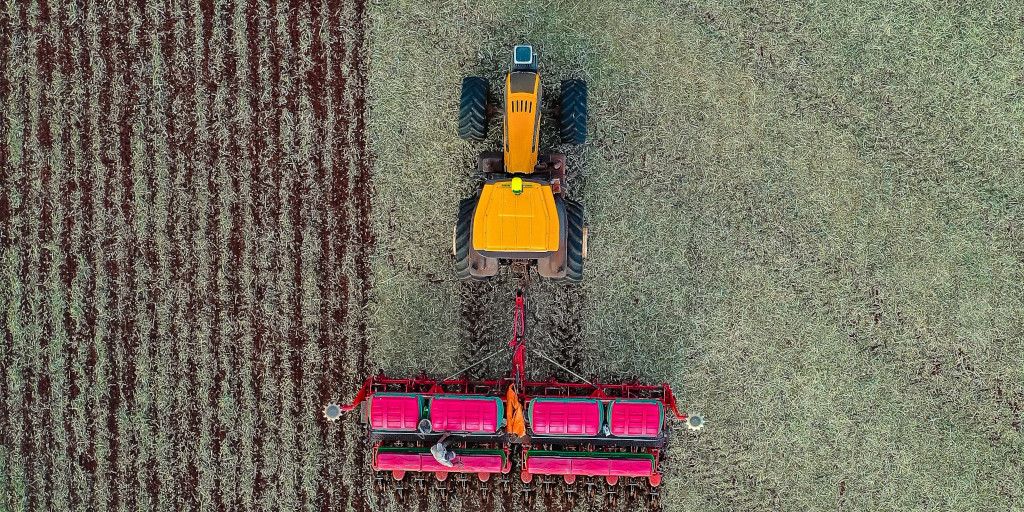 Overhead view of a field, an orange tractor pulls a plow