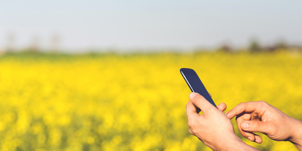 A farmer holds a smartphone in one hand, tapping something on the screen.
