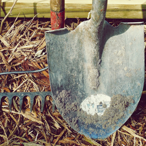 A shovel, a rake, and various handheld farm tools lean up against a bale of hay